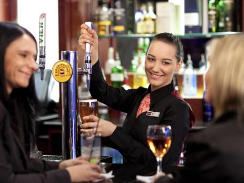 a woman is holding up a drink at a bar at Mercure Gloucester Bowden Hall Hotel in Gloucester