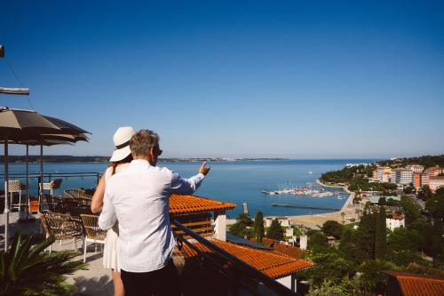 a man and woman standing on a balcony looking at the water at Villa Bellevue Portoroz-Portorose in Portorož
