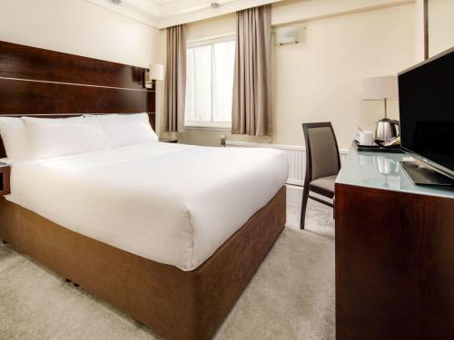 a bedroom with a bed and a desk and a television at Mercure Glasgow City Hotel in Glasgow