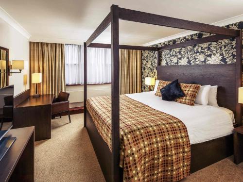 a hotel room with a canopy bed and a desk at Mercure Maidstone Great Danes Hotel in Maidstone