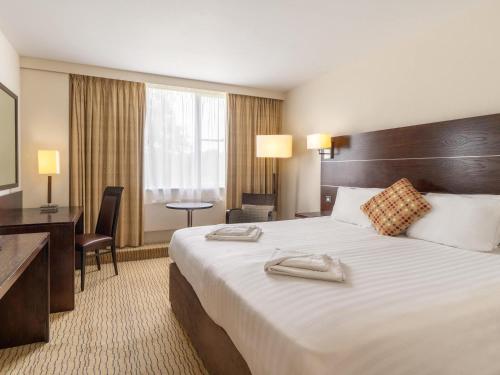 a hotel room with a large bed and a desk at Mercure Maidstone Great Danes Hotel in Maidstone
