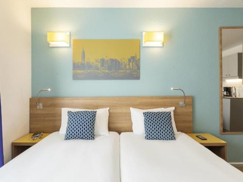 two beds in a room with blue walls and lamps at Aparthotel Adagio Access La Défense - Place Charras in Courbevoie