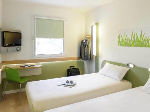 a room with two beds and a desk and a tv at Ibis budget Osnabrück City in Osnabrück