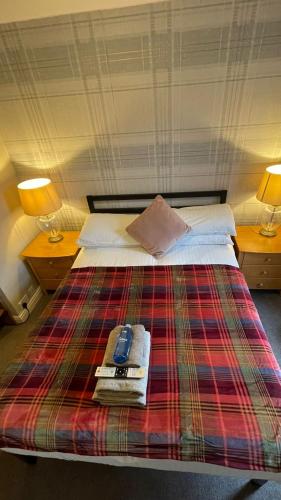 a bed with a plaid blanket and a cell phone on it at Autumn Leaves Guest House in Windermere