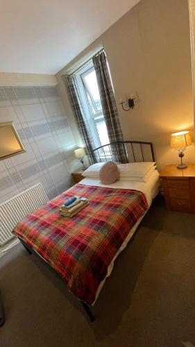 a bedroom with a bed with a plaid blanket and a window at Autumn Leaves Guest House in Windermere