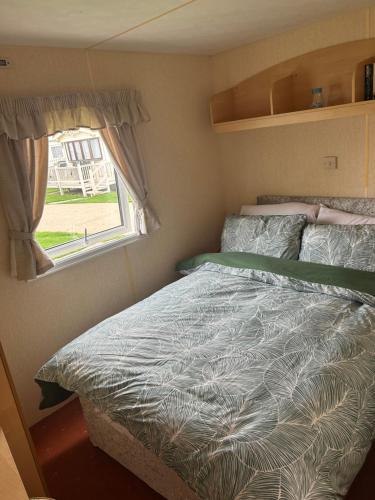 a bed in a small room with a window at Happy Days Caravan Park - Lovely Spacious 3 Bed Caravan in Chapel Saint Leonards