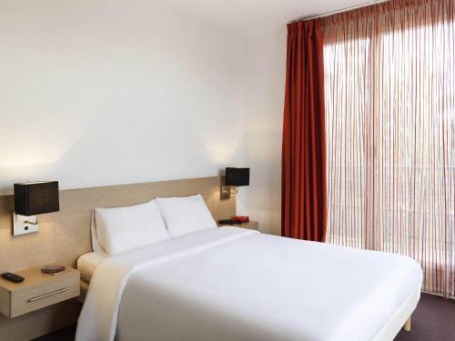 a bedroom with a large white bed and a window at Aparthotel Adagio Access Saint Louis Bâle in Saint-Louis