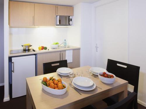 a kitchen with a table with a bowl of fruit on it at Aparthotel Adagio Access Saint Louis Bâle in Saint-Louis