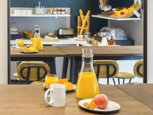 Una mesa con una jarra de jugo de naranja y platos de fruta. en Aparthotel Adagio Access Nantes Viarme, en Nantes