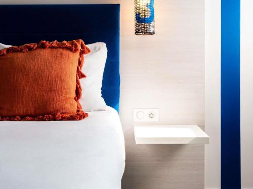 a bed with an orange pillow and a night stand at ibis Styles Quiberon Centre in Quiberon