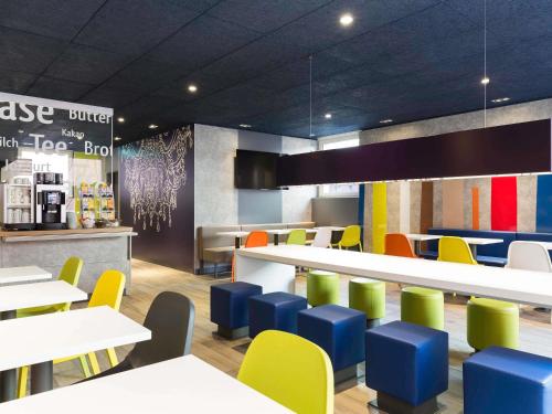 a restaurant with white tables and colorful chairs at ibis budget Zurich Airport in Glattbrugg