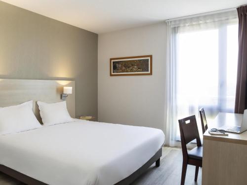 Schlafzimmer mit einem großen weißen Bett, einem Schreibtisch und einem Fenster in der Unterkunft Aparthotel Adagio Access Avignon in Avignon