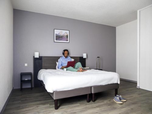 a woman sitting on a bed reading a book at Aparthotel Adagio Access Orléans in Orléans