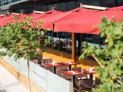 a row of tables with red umbrellas in front of a building at Novotel Sofia in Sofia