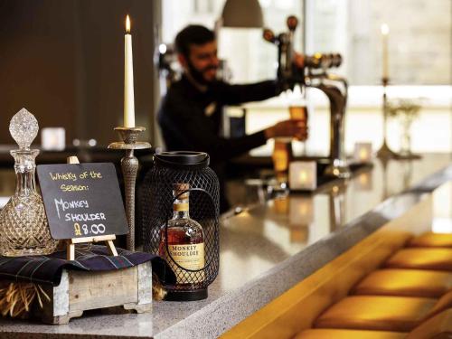 a man sitting at a bar with a bottle of whiskey at ibis Edinburgh Centre South Bridge – Royal Mile in Edinburgh