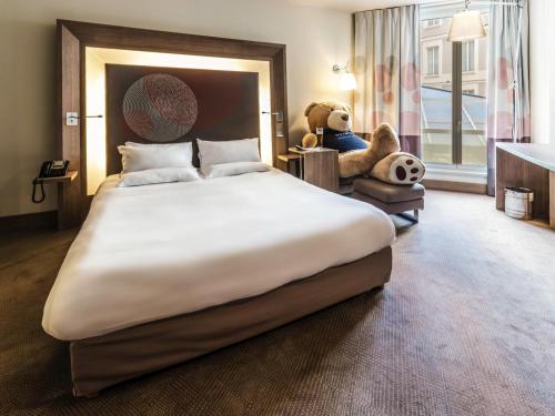 a large bed with a teddy bear sitting in a chair at Novotel Toulouse Centre Wilson in Toulouse