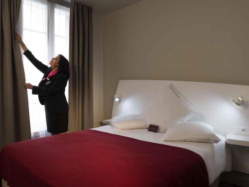 a woman is opening a window in a hotel room at Mercure Paris Levallois in Levallois-Perret