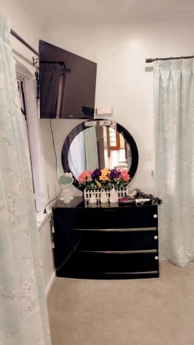 a black dresser with a mirror and flowers on it at Private Bedroom and Large Deck Separate Entrance in Auckland