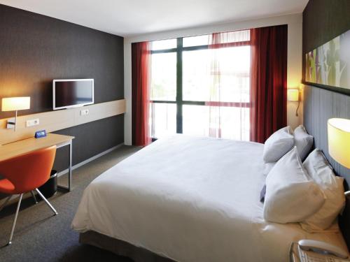 a hotel room with a bed and a desk and a television at Mercure Valenciennes Centre in Valenciennes