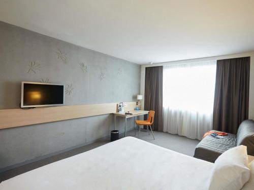 a hotel room with a bed and a tv on the wall at Mercure Valenciennes Centre in Valenciennes