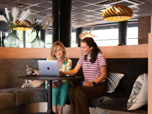 two women sitting at a table with a laptop at Mercure Valenciennes Centre in Valenciennes