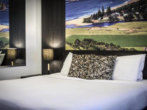a bedroom with a white bed with a painting on the wall at Mercure Gerringong Resort in Gerringong