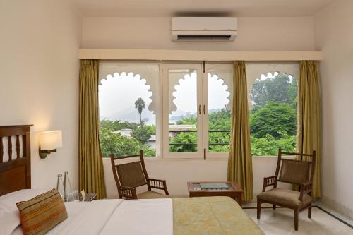 a bedroom with a bed and two chairs and a large window at Rampratap Palace by Fateh Collection in Udaipur