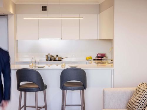a kitchen with two bar stools and a counter at The Sebel Quay West Suites Sydney in Sydney