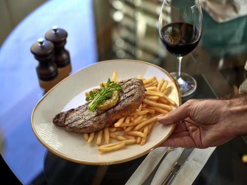 a plate of steak and french fries with a glass of wine at The Sebel Quay West Suites Sydney in Sydney