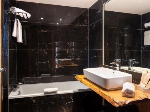 a black tiled bathroom with a sink and a tub at Mercure Brignoles Golf de Barbaroux & Spa in Brignoles