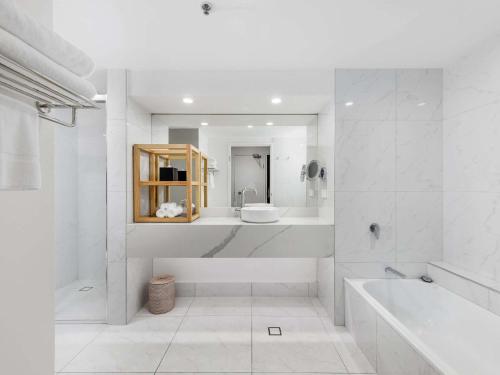 a white bathroom with a tub and a sink at Pullman Cairns International in Cairns