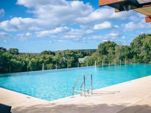 a swimming pool with blue water and trees in the background at Pullman Bunker Bay Resort Margaret River in Dunsborough