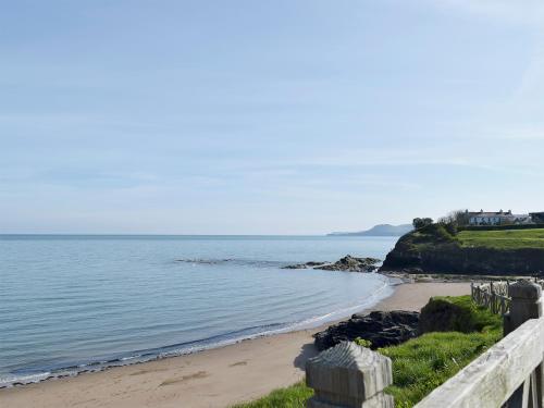 a beach with a fence next to the ocean at Woodpecker Rest in Cilgerran