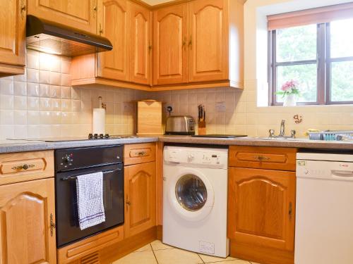 a kitchen with wooden cabinets and a washer and dryer at Beudy Mawr - 16985 in Brynsiencyn