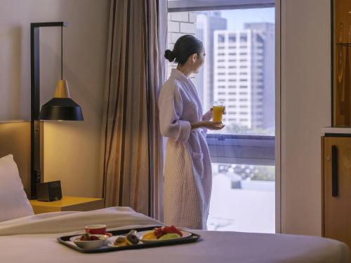 a woman standing in a hotel room with a tray of food at Mercure Brisbane King George Square in Brisbane