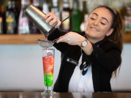 a woman is making a drink at a bar at Pullman Magenta Shores Resort in The Entrance