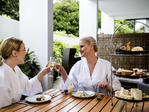 two women sitting at a table with glasses of wine at Pullman Magenta Shores Resort in The Entrance