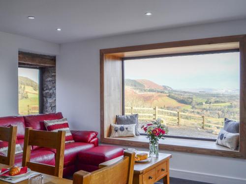 a living room with a red couch and a large window at Pistyll Gwyn in Llanwrthwl