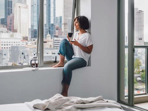 a woman sitting on a window sill holding a cell phone at Quay West Suites Melbourne in Melbourne