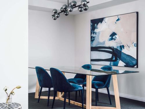 a dining room with a glass table and blue chairs at Quay West Suites Melbourne in Melbourne