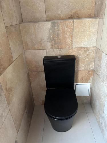 a bathroom with a black toilet in a tile wall at Le meublé du Sable Nwar in Étang-Salé