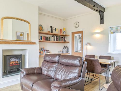 a living room with a leather couch and a fireplace at Seascape Cottage in Allonby