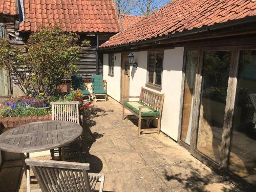 un patio con tavolo, sedie e una casa di The Old Cow Shed a Thorndon