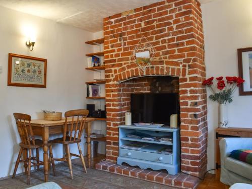 a living room with a brick fireplace with a tv at Poppy Cottage in Halesworth