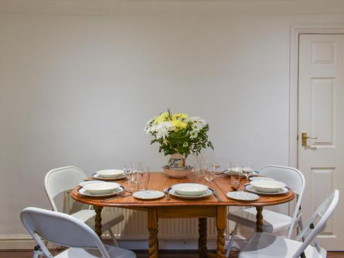 a wooden table with white chairs and a table with flowers at Coast To Coast Cottage in Cleator Moor