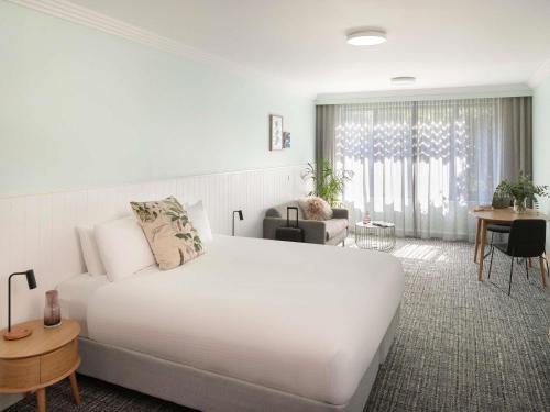 a bedroom with a large white bed and a living room at The Sebel Kiama in Kiama