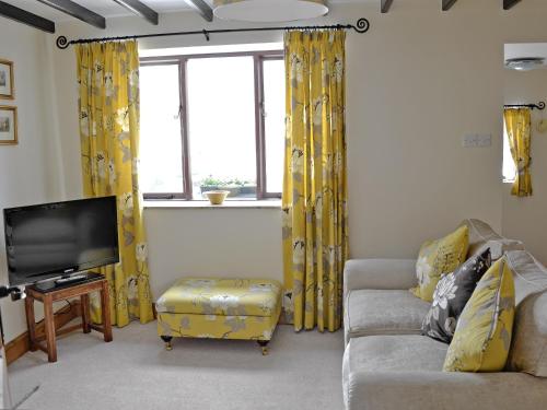 - un salon avec des rideaux jaunes, un canapé et une télévision dans l'établissement Rundales Cottage, à Appleby