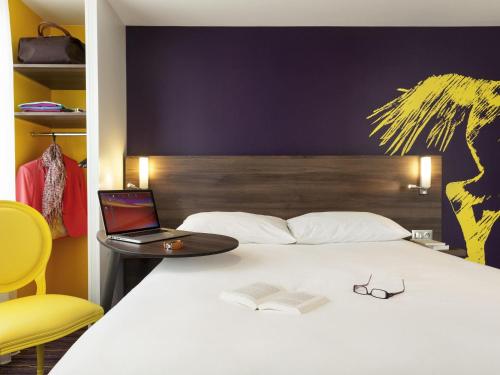 a bed with a laptop and a table with a book at ibis Styles Saumur Gare Centre in Saumur