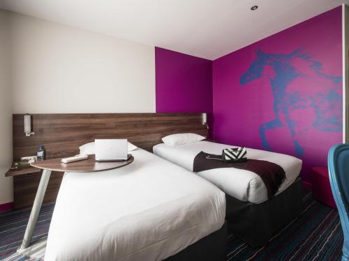 two beds in a hotel room with a purple wall at ibis Styles Saumur Gare Centre in Saumur