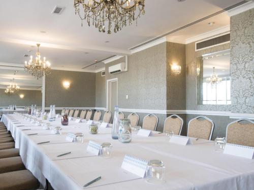 a meeting room with white tables and chairs and a chandelier at Mercure Milton Keynes Hotel in Milton Keynes